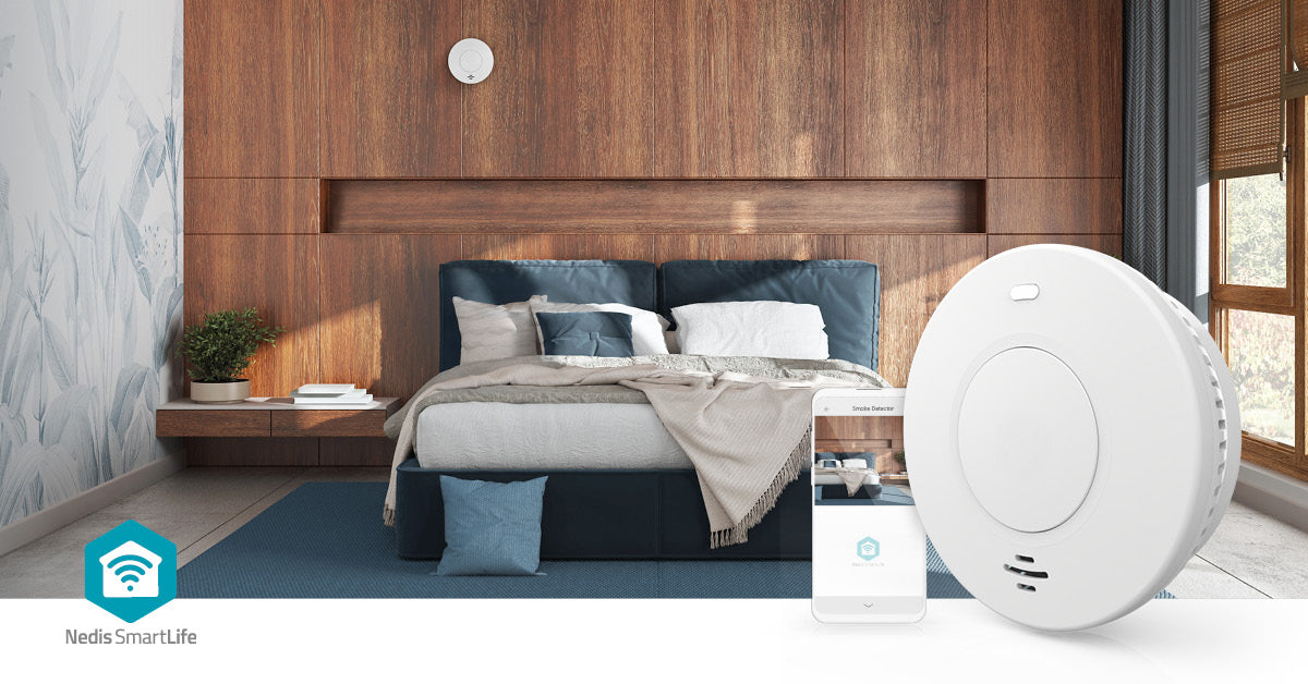 Nedis WiFi brandalarm 10 år og smartphone med app vises i soveværelse, produkterne tydeligt i forgrunden.