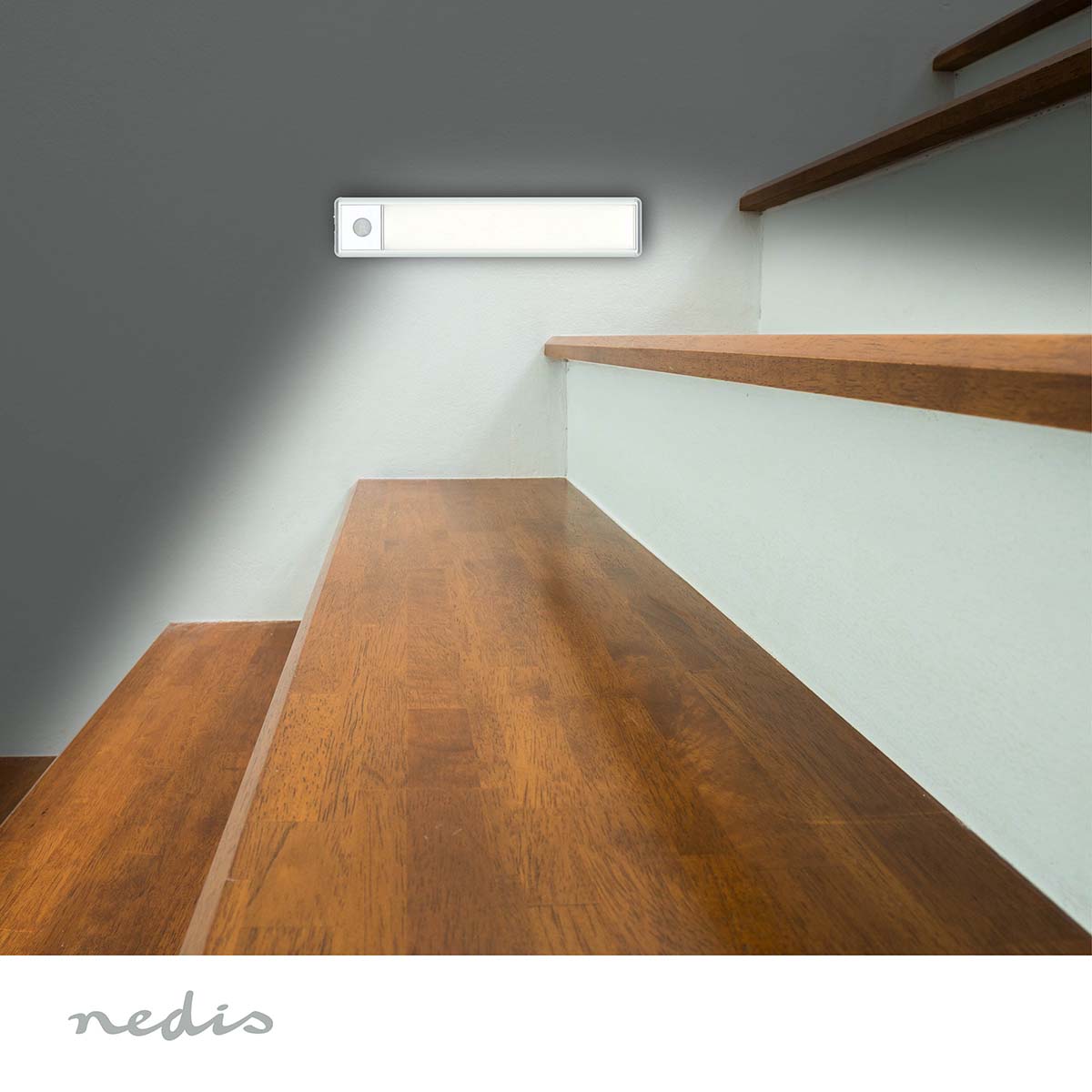 Nedis LED skabslampe 20cm med bevægelsessensor monteret over trappe med hvide stødtrin, Nedis-logo nederst.