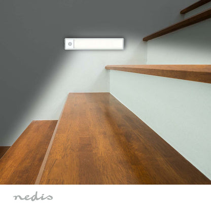 Nedis LED skabslampe 20cm med bevægelsessensor monteret over trappe med hvide stødtrin, Nedis-logo nederst.