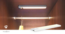 Nedis LED skabslampe 20cm med bevægelsessensor, monteret i loft på træskab, close-up af lampe og Nedis-logo.