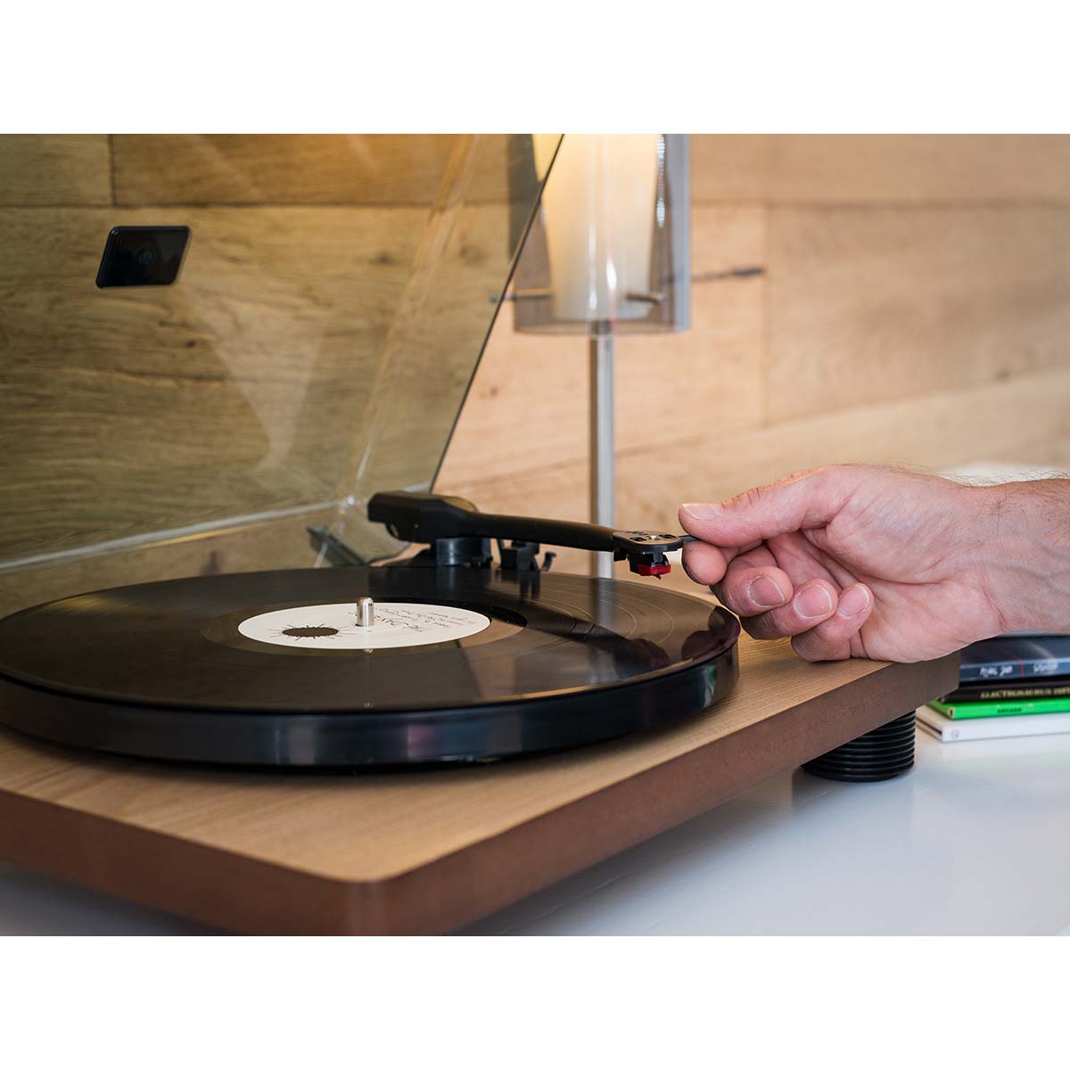 Lenco LS-50 pladespiller med indbyggede højttalere, vinylplade på træbord, hånd justerer tonearm.