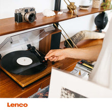 Lenco Pladespiller med Bluetooth, justeres ved nålen, orange Lenco-logo nederst, placeret på træhylde.