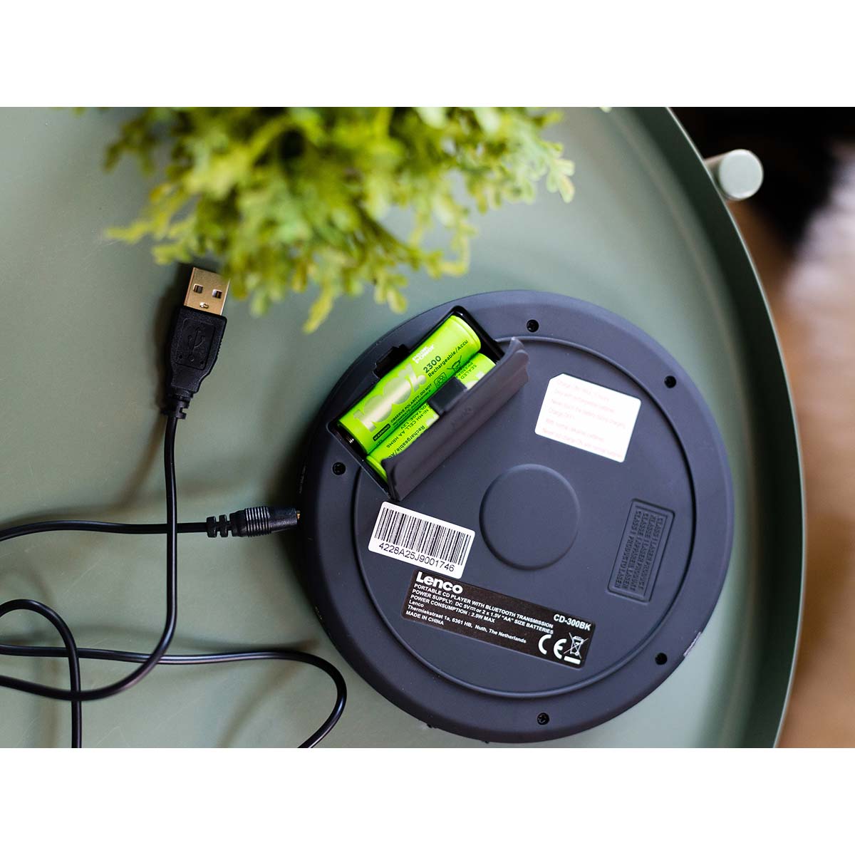 Lenco bærbar Bluetooth CD-MP3-afspiller Sort med åben batterirum, 2 grønne AA-batterier, tilsluttet USB-kabel.