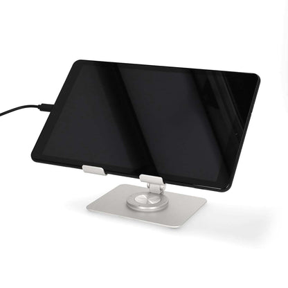 Tablet med sort skærm på sølv tabletstativ, tilsluttet opladerkabel.