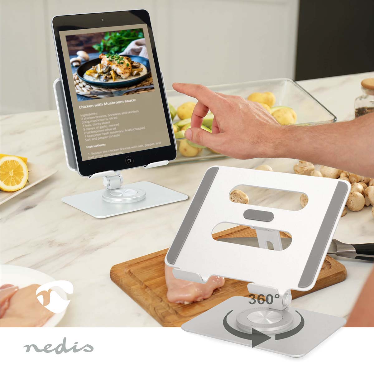 Tabletstativ Sølv, justerbar tabletholder på roterende metalfod, brugt på køkkenbord med madlavning i gang.