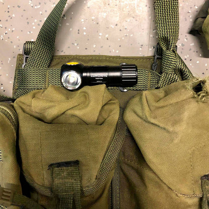 Grøn taktisk vest med to store lommer, sort Lumonite Vector V2 pandelampe 500 lm fastgjort på remmen.