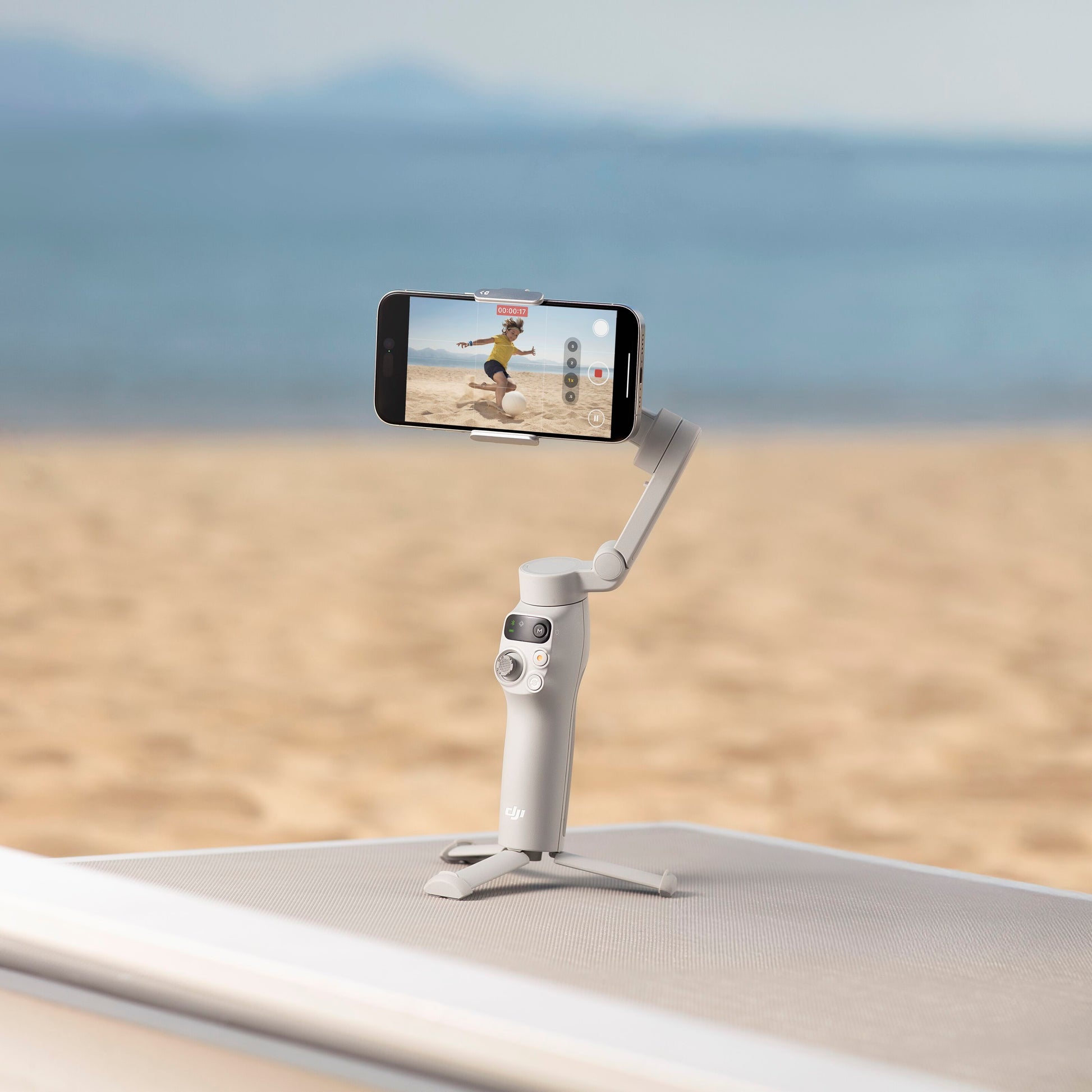 DJI Osmo Mobile 7 Gimbal til smartphone på sandstrand optager stabiliseret video af hav og himmel.