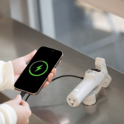 DJI Osmo Mobile 7 grå gimbal med smartphone forbundet via kabel, opladningssymbol synligt på telefonen.