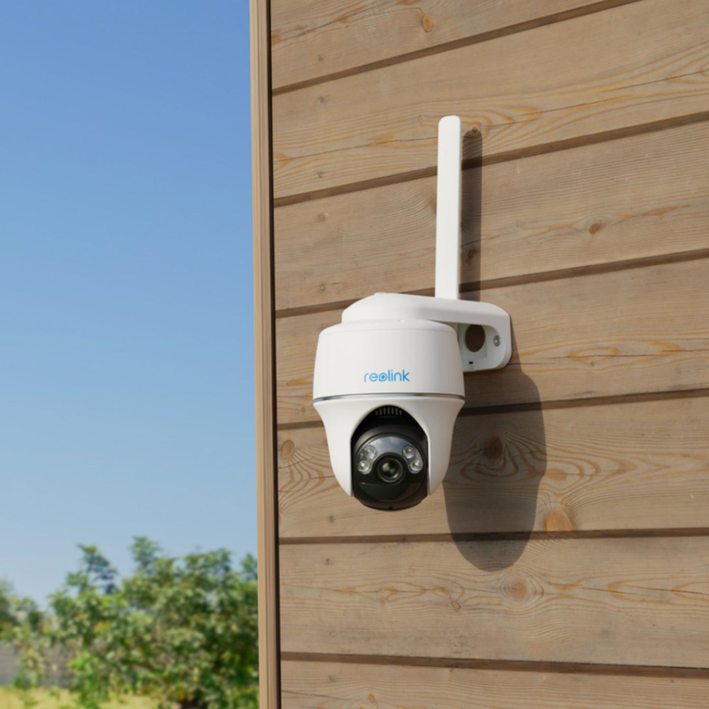 Reolink Go Series G430 udendørs 4G LTE kamera 2K monteret på trævæg med blå himmel og grønne træer bagved.
