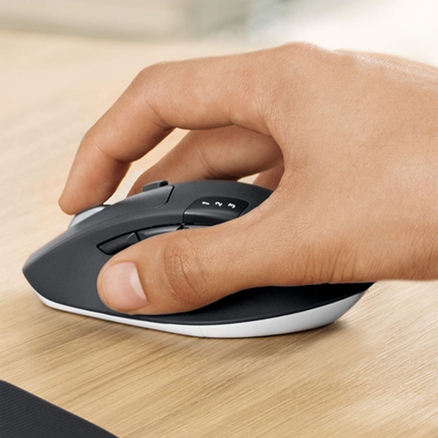 Logitech MK850 trådløs sort/hvid mus med hånd på venstre knap, ses på lys træbord sammen med MK850 tastatur.
