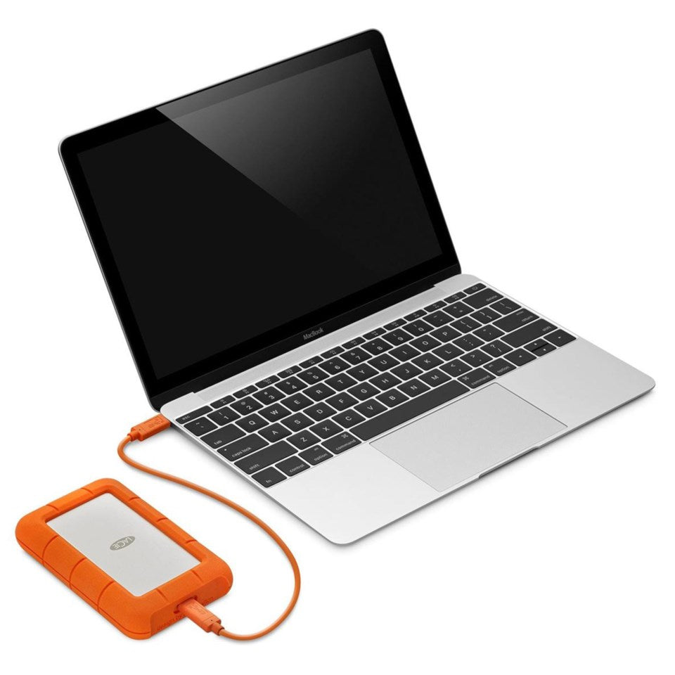 Lacie Robust ekstern harddisk 4TB tilsluttet sølvfarvet laptop med sort tastatur via orange USB-C-kabel, skærm er slukket.