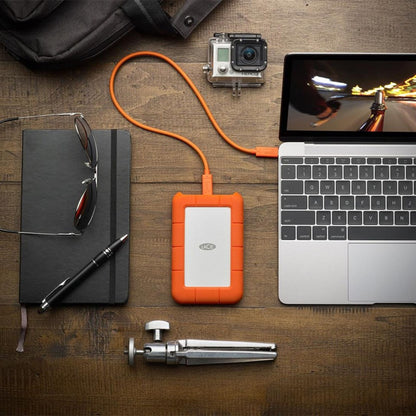 Lacie Robust ekstern harddisk 4TB USB-C tilsluttet laptop, synlig sammen med notebook, pen, briller, mini-stativ, actionkamera.