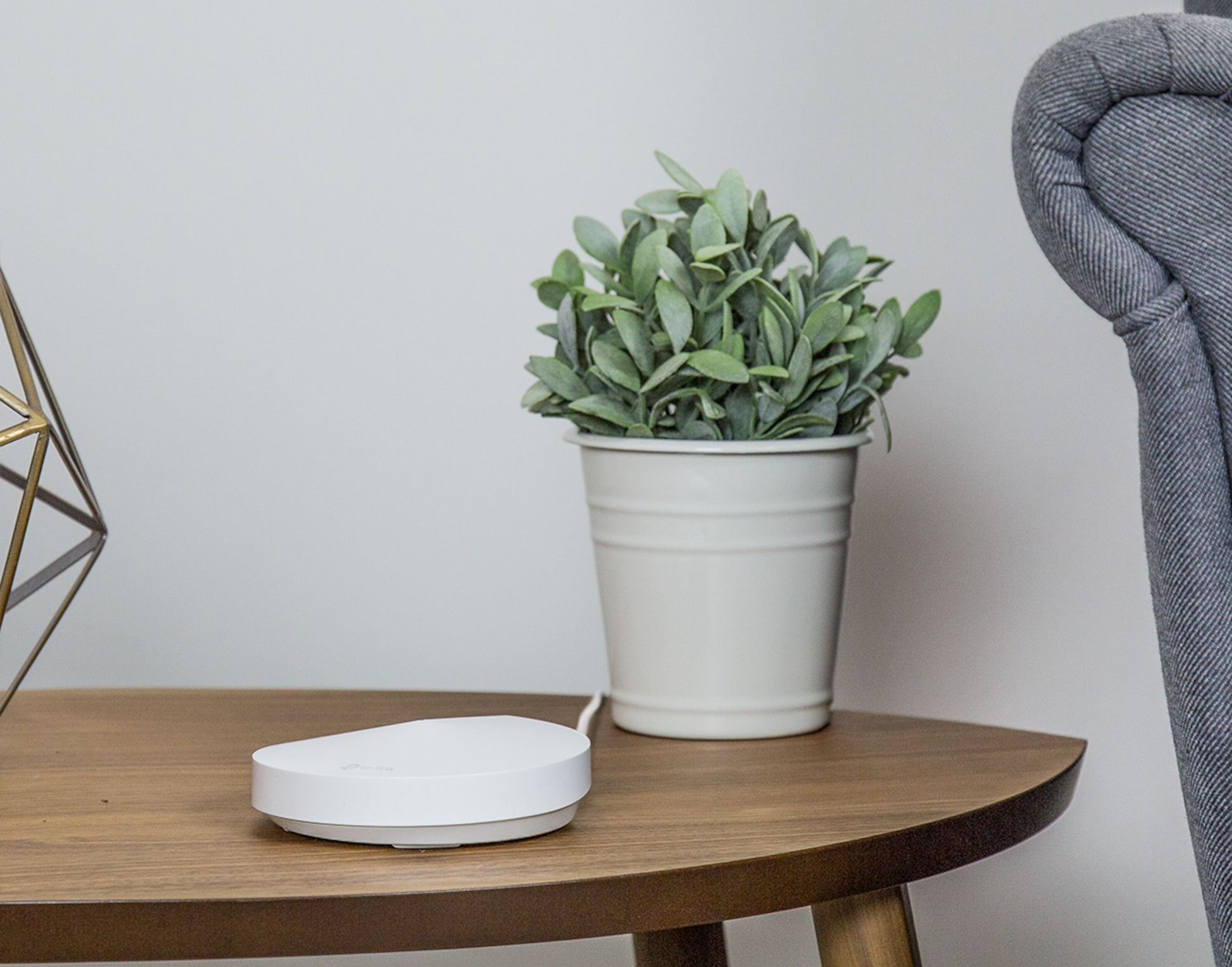 TP-Link Deco M5 Mesh-node AC1300 hvid på træbord ved grøn plante og grå stol.
