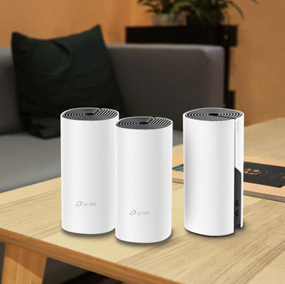 TP-Link Deco M4 Mesh AC1200 router 3-pak i hvid på lyst træbord, grå sofa og puder synlige i baggrunden.