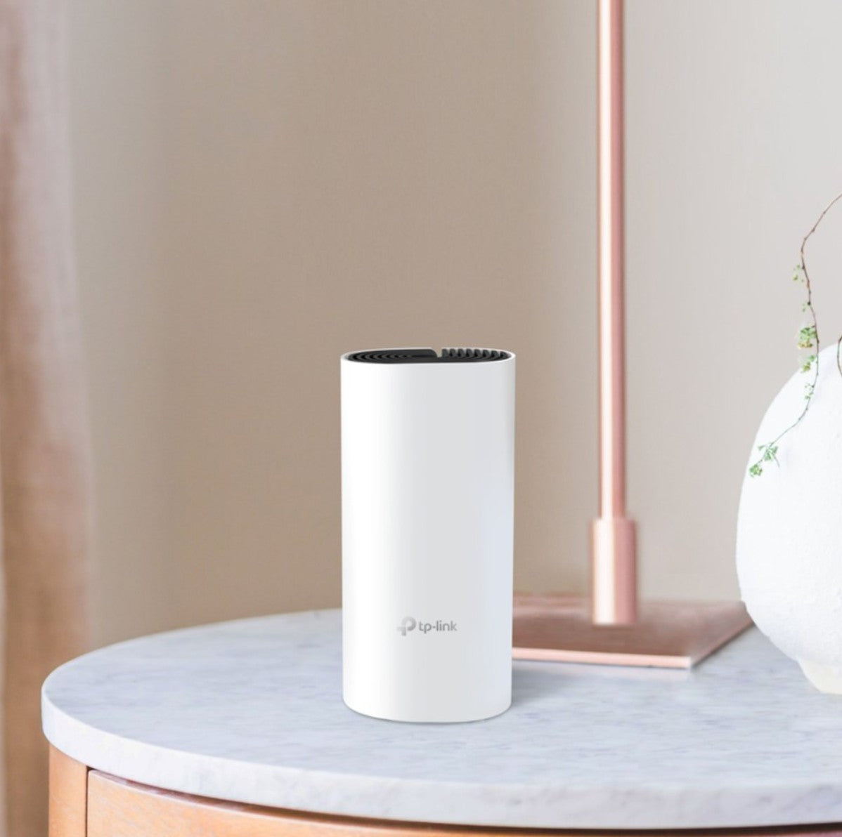 TP-Link Deco M4 Mesh-system AC1200 3 stk hvid cylinder med sort ventileret top på marmorbord ved rosaguld lampe.