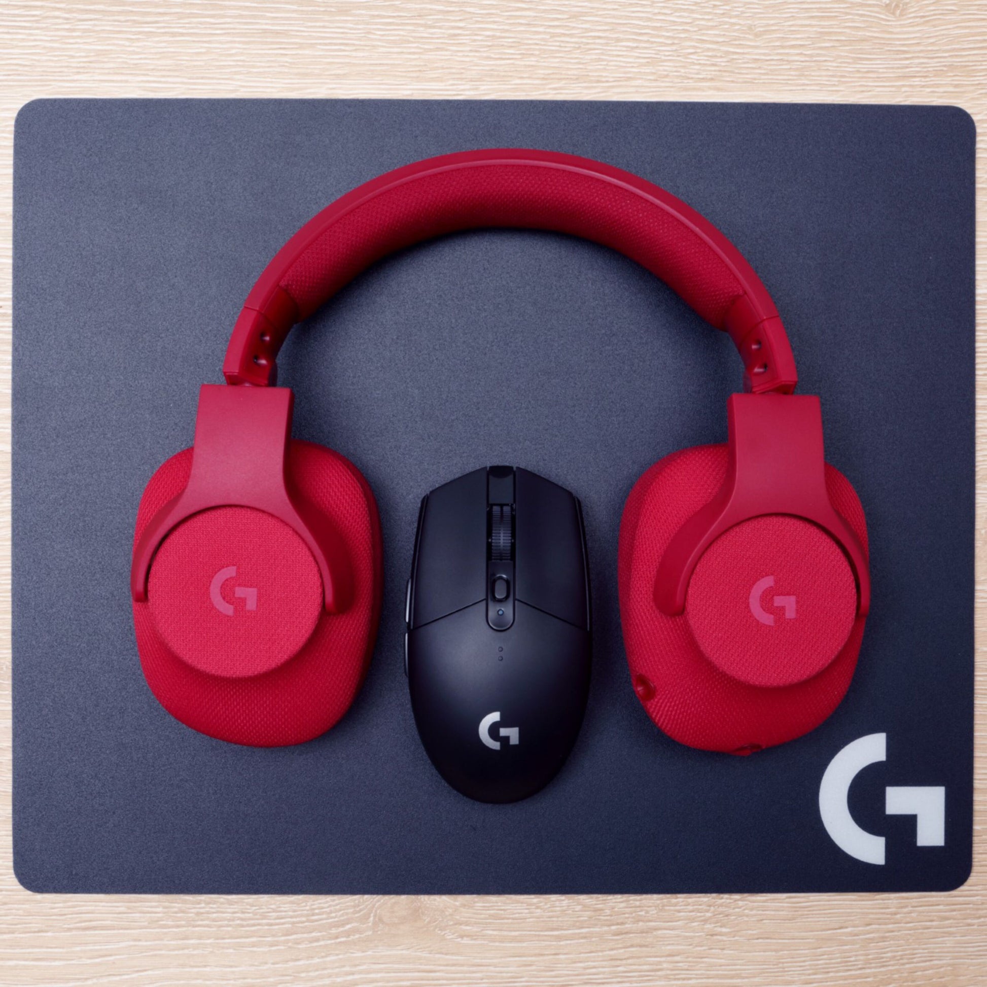 Røde over-ear hovedtelefoner og sort Logitech G305 Lightspeed trådløs gamingmus på sort Logitech musemåtte.