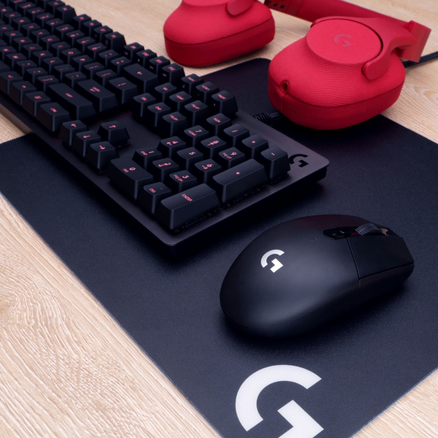 Logitech sorterer gamingtastatur, mus og musemåtte med hvidt G-logo samt røde over-ear hovedtelefoner, G305 Lightspeed mus.