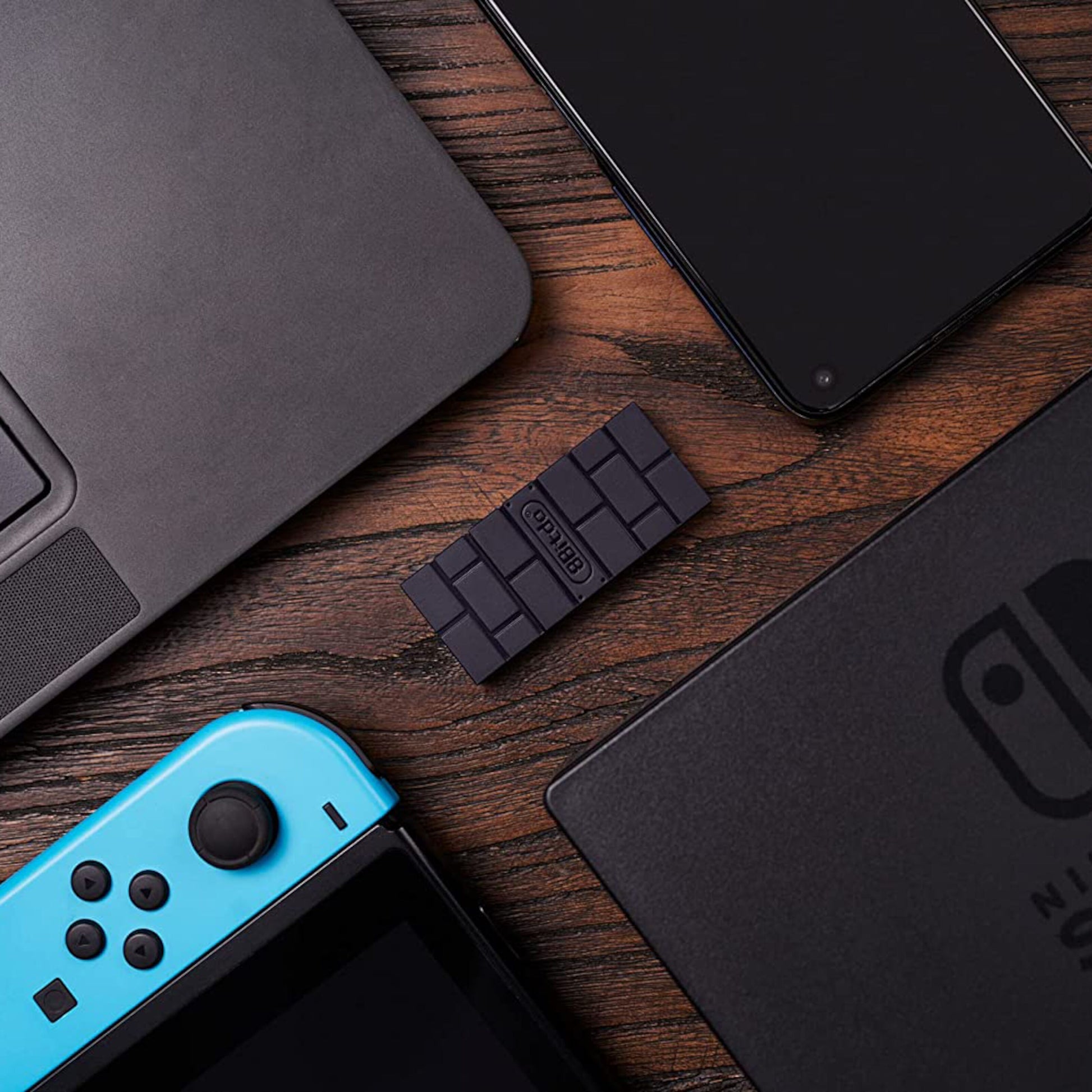 Sort fidgetlegetøj formet som chokolade ved siden af laptop, smartphone, Nintendo Switch og 8Bitdo Trådløs USB-adapter 2.