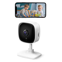 TP-Link Tapo C100 trådløst overvågningskamera vist under smartphone med live-billede af børn, der leger på gulvet.