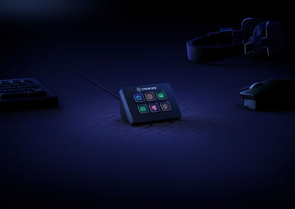 Elgato Stream Deck Mini programmerbart tastatur på sort bord med USB-tastatur, mus og hovedtelefoner i blåt lys.
