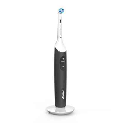 Jordan Clean Smile Plus elektrisk tandbørste sort/hvid, synlig power-knap og rund børstehoved på hvid opladerbase.
