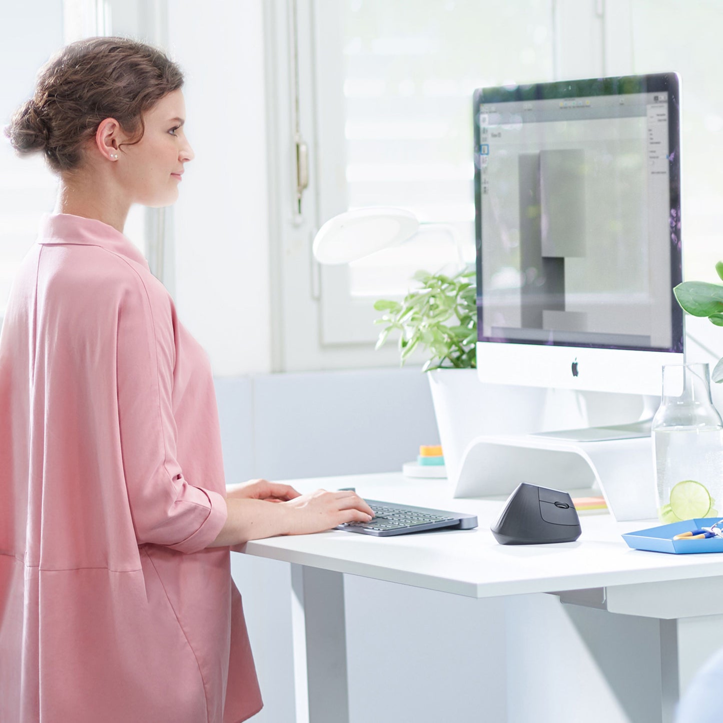 Logitech MX Vertikal trådløs mus til computer på skrivebord med tastatur og stor skærm i lyst kontormiljø.