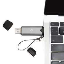 Plexgear Hukommelseskortlæser til SD og Micro-SD sølv med sort hætte og strop, tilsluttet laptop USB-port, løse hætter ved siden af.