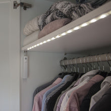 Luxorparts LED-liste med bevægelsessensor 1 m under hylde, foldede trøjer øverst, skjorter/jakker hængende nedenunder.