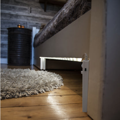 Luxorparts LED-liste med bevægelsessensor 1 m under seng, trægulv, gråt rundt tæppe, metalnatbord, trævæg.