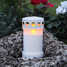 Gravlys med LED og glødende flamme blandt mos og grene, grønne planter og hvide blomster taske, lang batterilevetid.