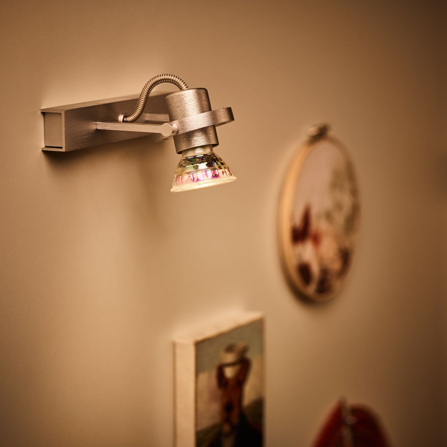 Spotlight i metal til væg med GU10 LED-pære 345 lm, varm hvidt lys mod beige væg og slørede indrammede billeder.