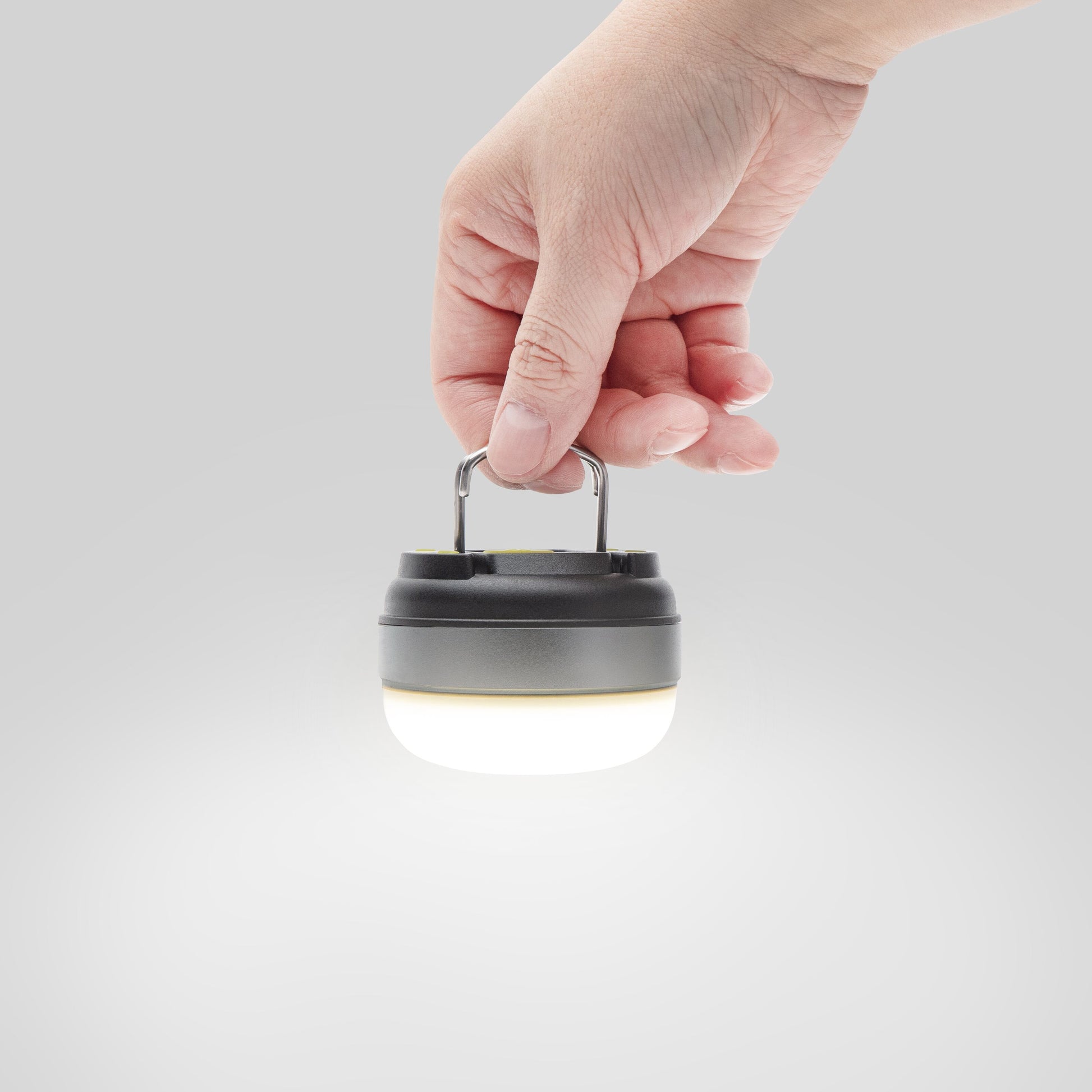 Ledsavers Mini-campinglampe LED, kompakt model med metalhåndtag, blødt hvidt lys, ses i hånd mod lys grå baggrund.