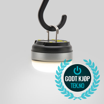 Ledsavers Mini-campinglampe hænger fra krog med blåt GODT KJØP TEK.NO logo med strømsymbol i forgrunden.