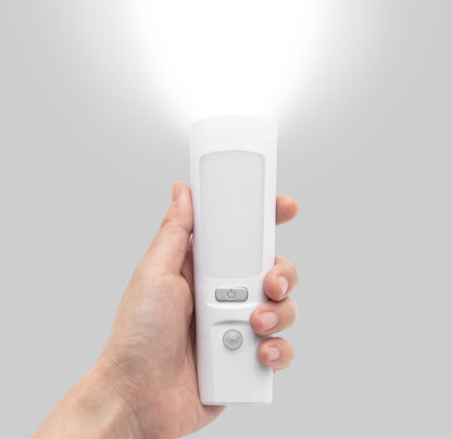 Luxorparts genopladelig lommelygte og natlampe tændt, holdes i hånd, grå baggrund.