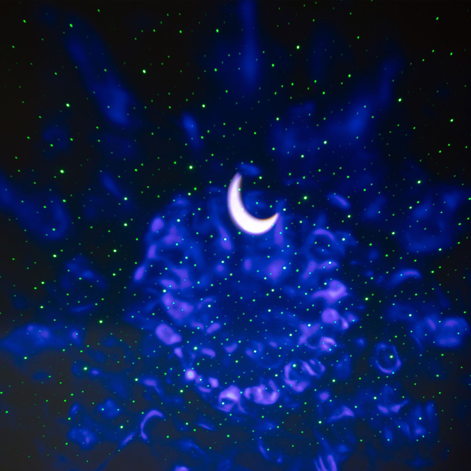 Rubicson natlampe med stjernehimmel projicerer glødende halvmåne, blå og lilla lys samt grønne laserprikker i mørke.
