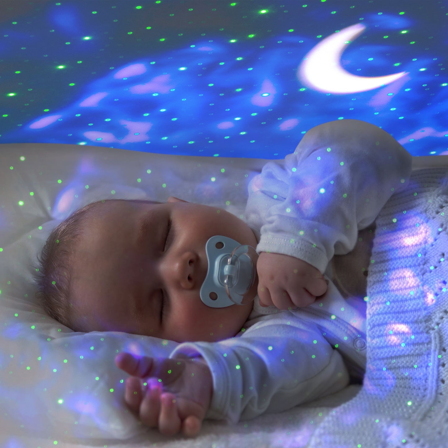 Rubicson Natlampe med stjernehimmel projicerer blå og grønne måne- og stjernelys natlampe, baby med sut under tæppe.