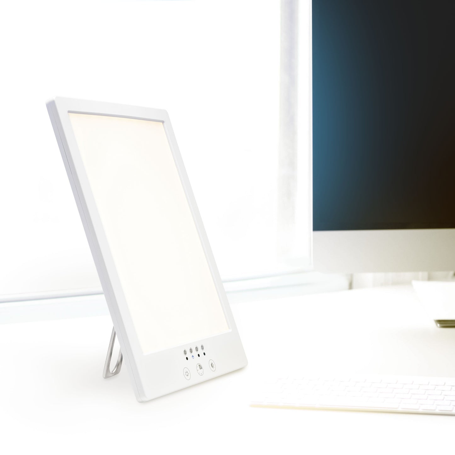 Rubicson Terapilampe 12.000 lux UV-fri, hvid, placeret ved siden af computerskærm og tastatur på skrivebord.