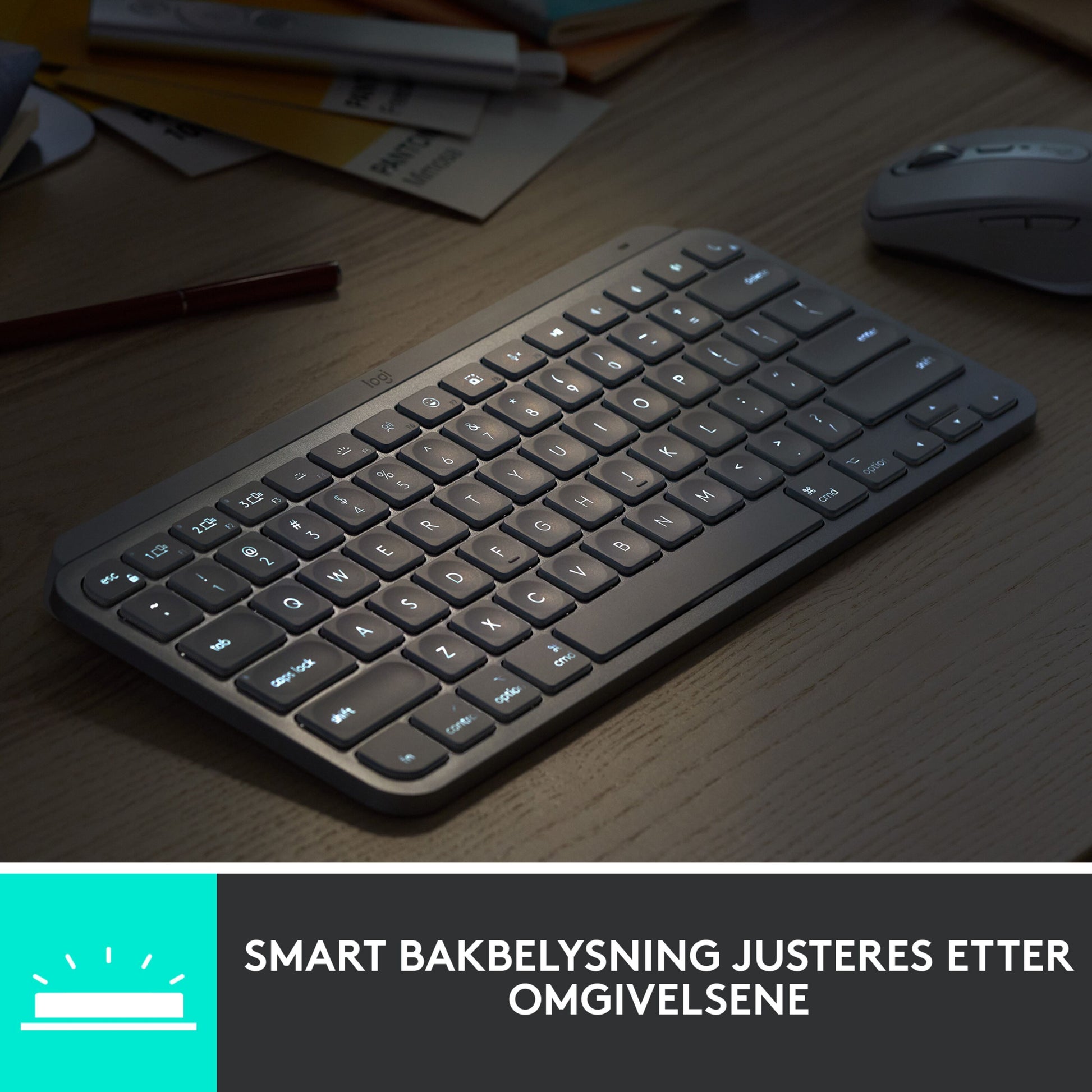 Logitech MX Keys Mini trådløst tastatur grå på bord ved mus og papirer, tekst: SMART BAKBELYSNING JUSTERES EFTER OMGIVELSERNE.