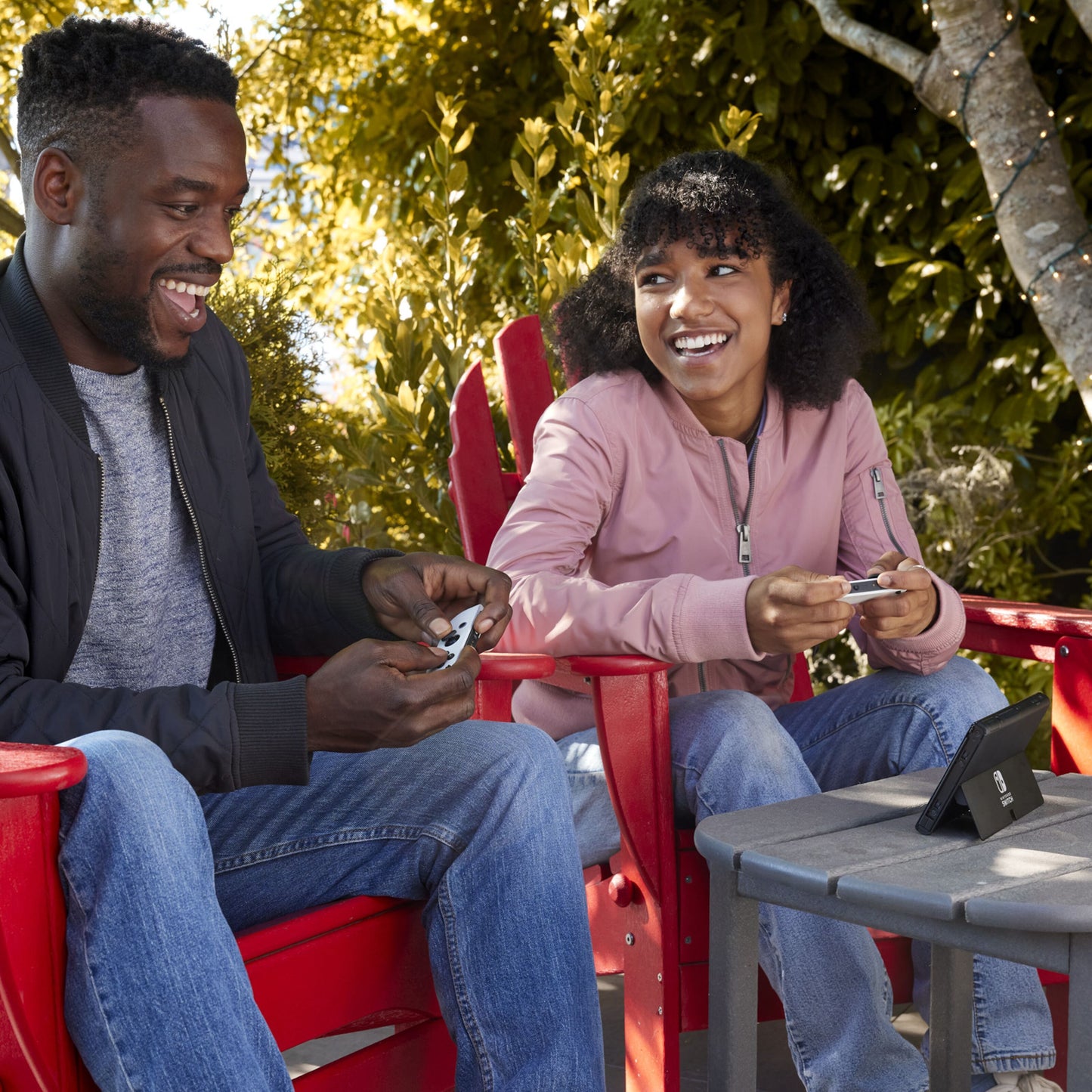 Nintendo Switch OLED håndholdt spillekonsol 7" rød/blå, Joy-Con controllere i brug udendørs.