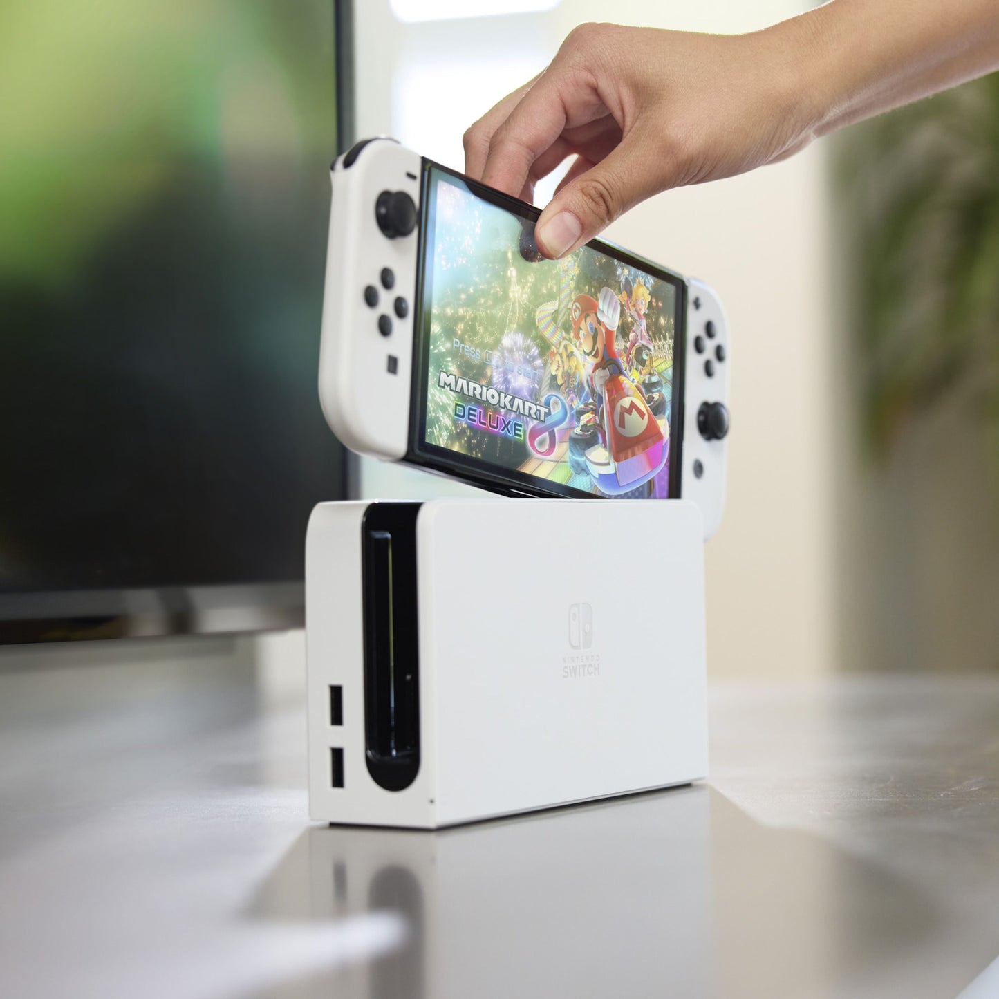 Nintendo Switch OLED 7" rød/blå vises med Mario Kart 8 Deluxe på skærmen i dockingstation.