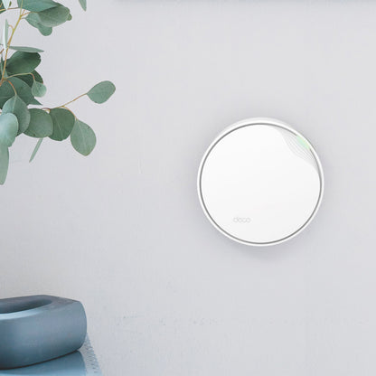 TP-Link Deco X50-PoE AX3000 mesh WiFi 6 i hvid, rund enhed med grøn LED, vægmonteret ved lyseblade og grå keramik.