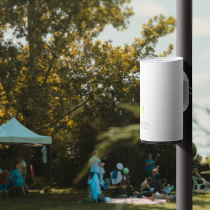 TP-Link Deco X50-Outdoor PoE AX3000 Mesh monteret på stang i park, Wi-Fi 6, folk og telte sløret i baggrunden.