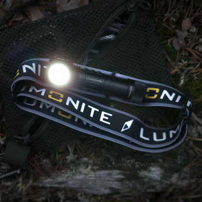 Lumonite Kompas sort pandelampe 1250 lm, IP69, synligt hvidt logo, på grøn netpose med blad og kviste.