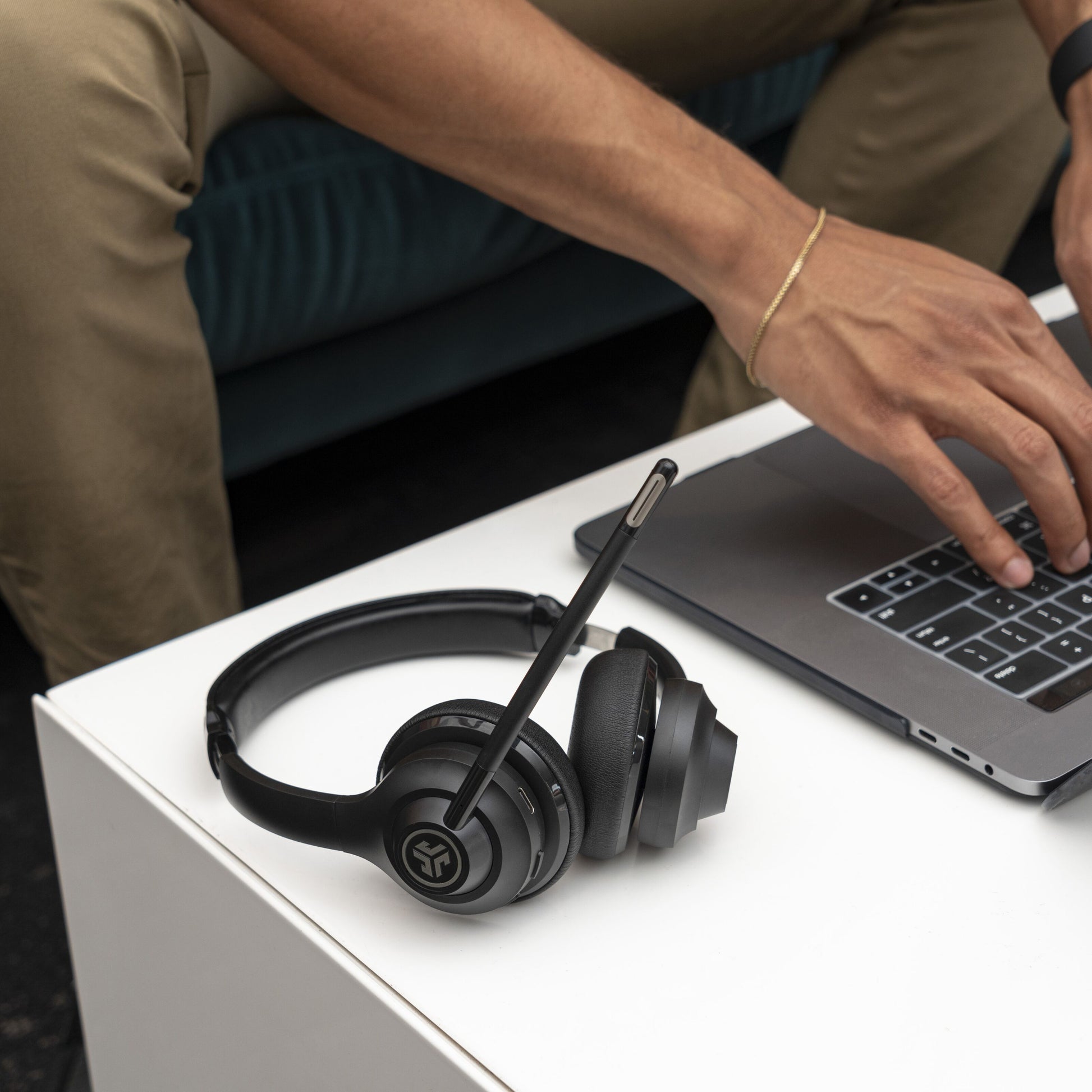 JLab GO Arbejde Trådløst headset med mikrofon og 45 timers batteritid på bord ved person der skriver på laptop.