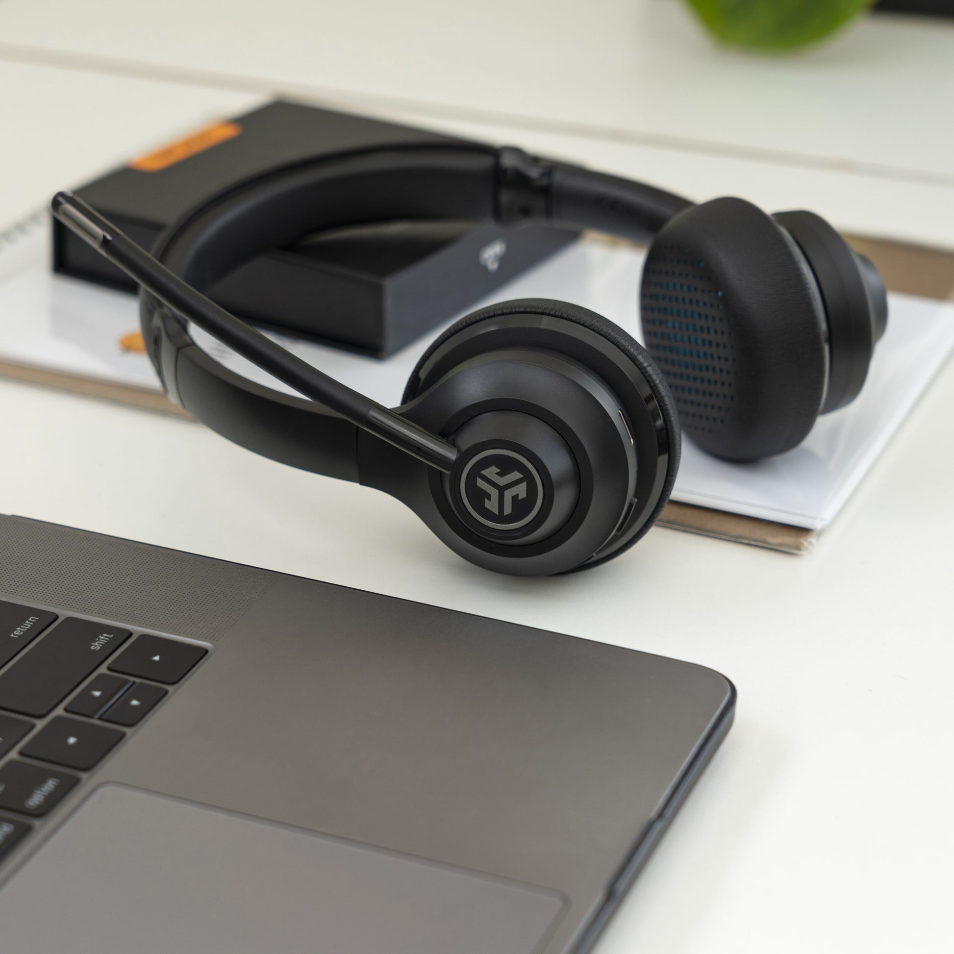 Jlab GO Arbejde trådløst headset sort med mikrofon og 45 timers batteritid på skrivebord ved bærbar, notesbøger, orange æske.