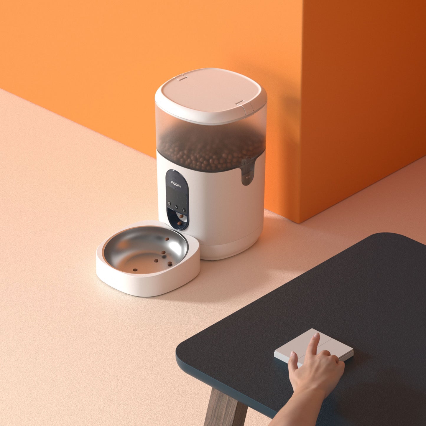 Aqara Smart kæledyrsfoderautomat C1 med tørfoder, knap trykkes, tom metalskål ved siden af, lys gulv, orange væg.