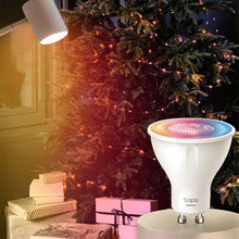 TP-Link Tapo L630 Smart RGB LED-pære GU10 lyser ved et juletræ med lyskæder og gaver, smart home kontekst.