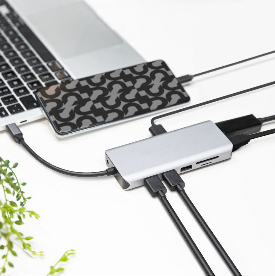 Plexgear USB-C Multiadapter 12 porte 100W tilsluttet laptop med flere kabler, smartphone i geometrisk cover ovenpå.