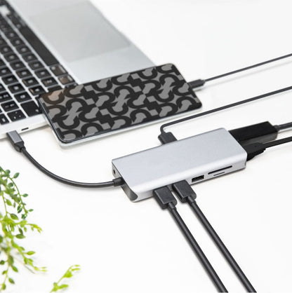 Plexgear USB-C Multiadapter 12 porte 100W tilsluttet laptop med flere kabler, smartphone i geometrisk cover ovenpå.