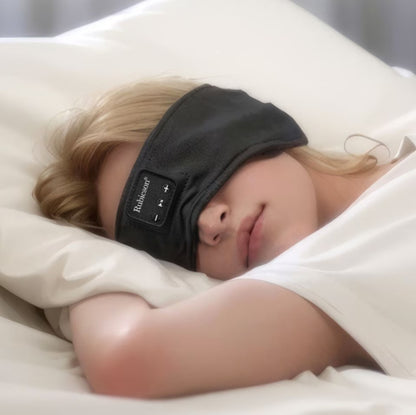 Blond person med Rubicson Bluetooth Sovemaske over øjnene på hvide lagner.
